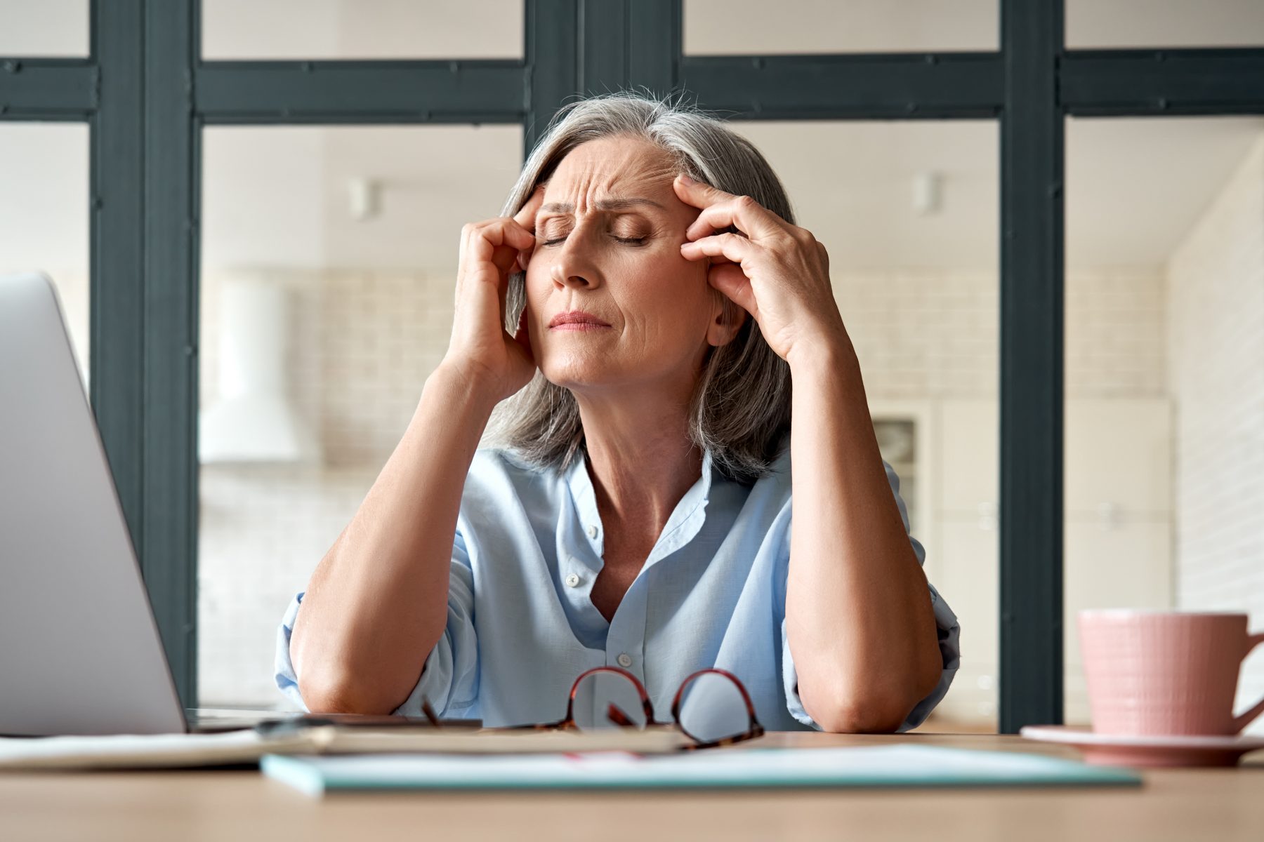 Tired stressed old mature business woman suffering from headache at work.