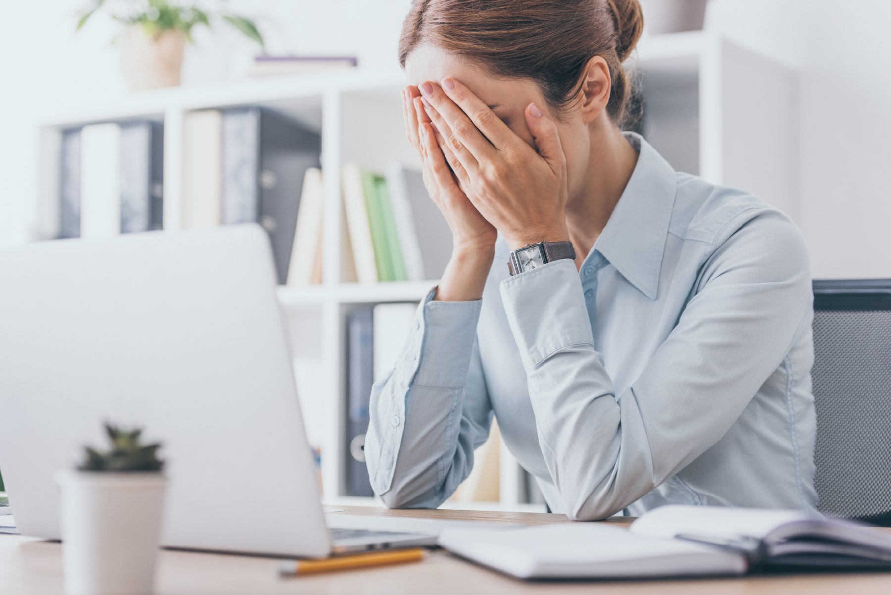 Woman with fatigue with her face in her hands in front of her laptop