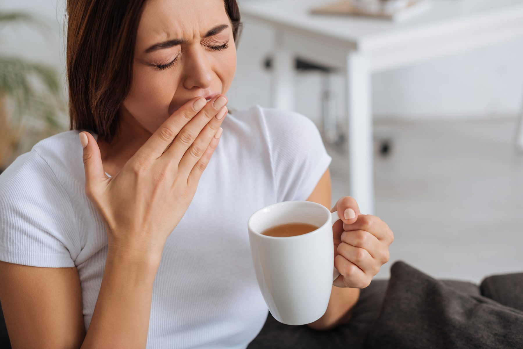 Fatigued woman yawning while drinking coffee