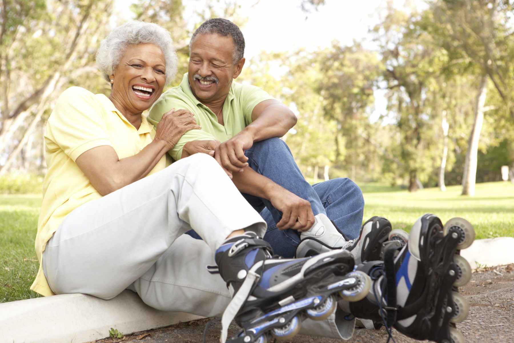 Senior Couple Putting On In Line Skates In Park and laughing together