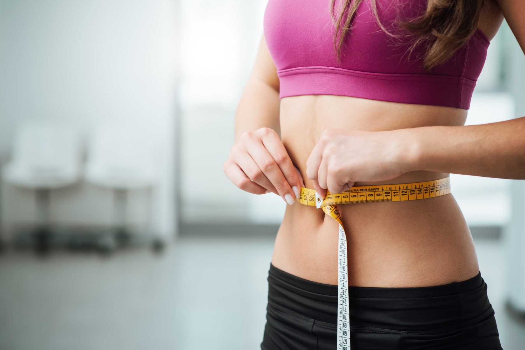 Woman with flat abs measuring her stomach with measuring tape
