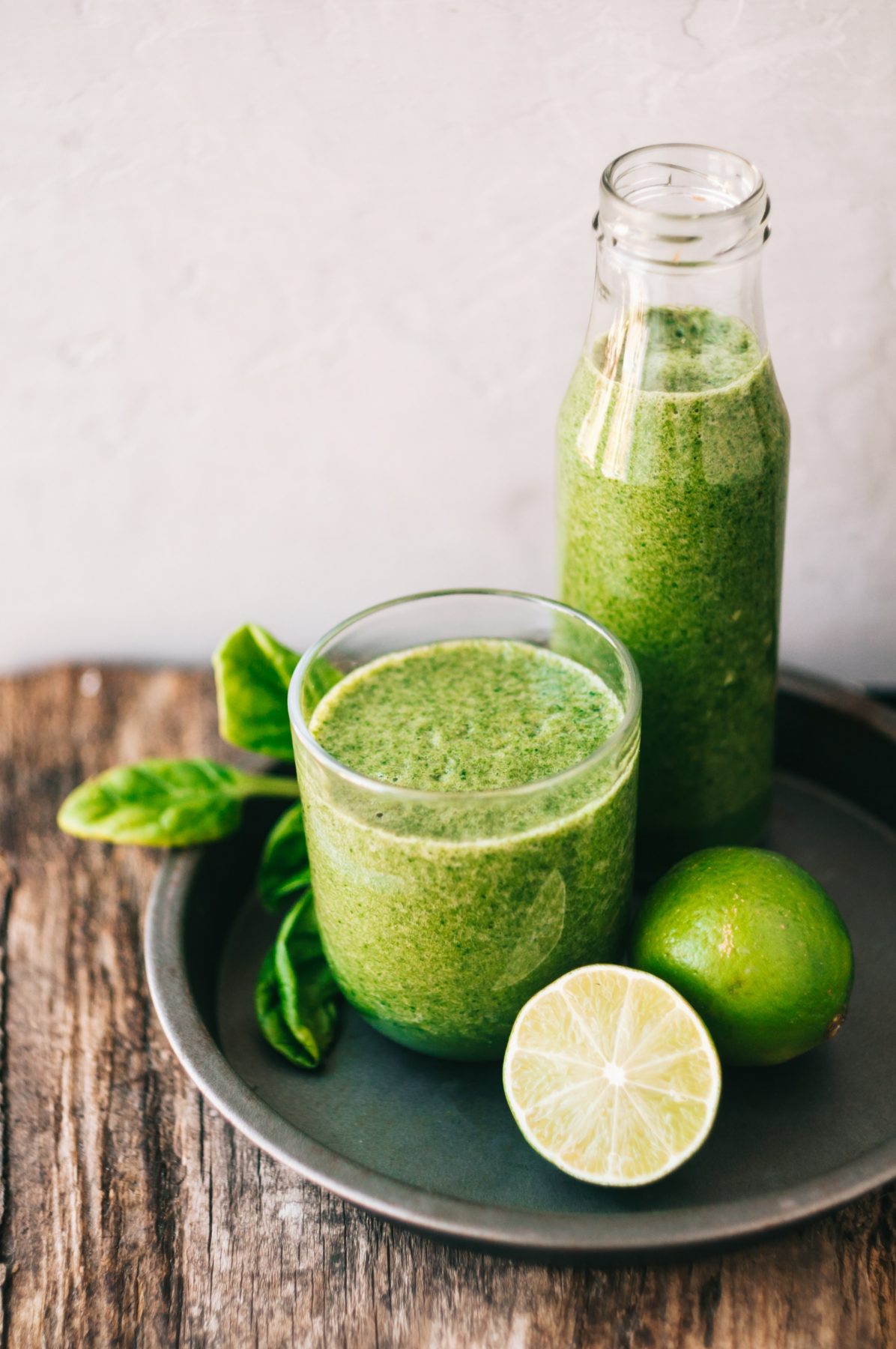 Green detox smoothie in glass and bottle and tray with limes
