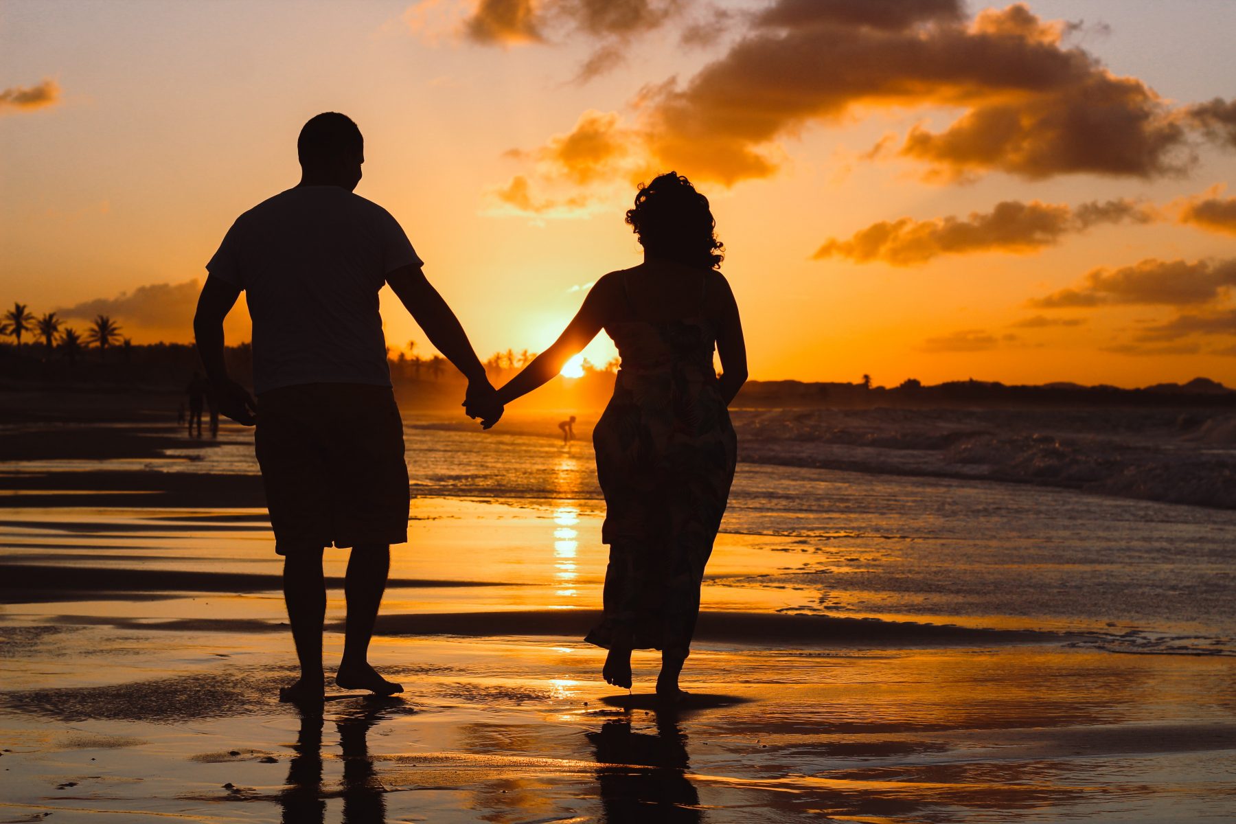 Older couple walking together holding hands on a beach at sunset