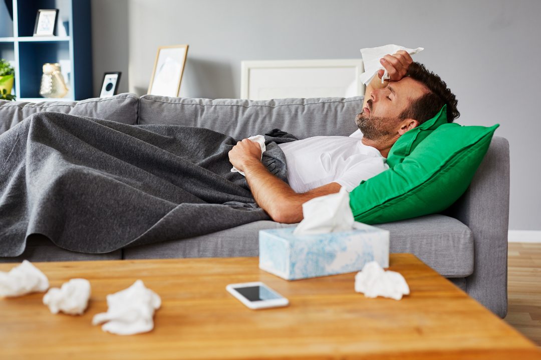 Sick man lying on sofa with used tissues around him